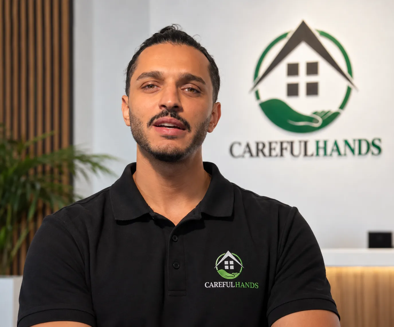 Orhan Demirovic, Geschäftsführer von Careful Hands, vor dem Careful-Hands-Logo.